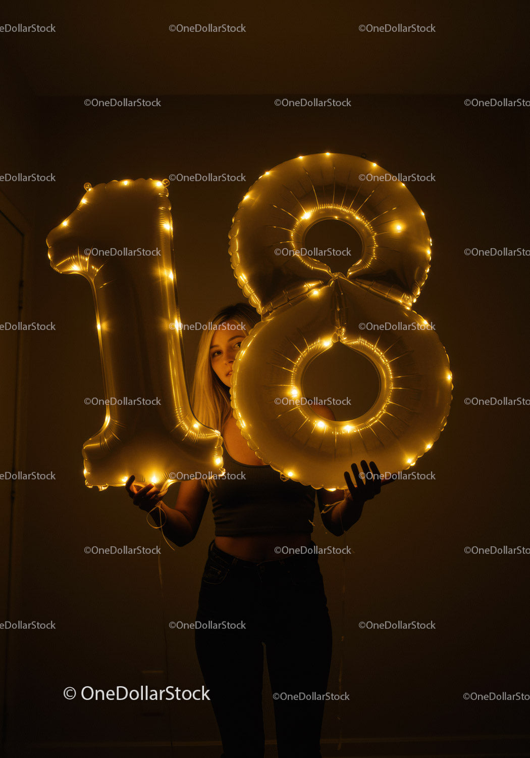 Young woman holding glowing 18 birthday balloons indoors