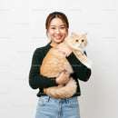 Smiling woman holding fluffy cream cat indoors