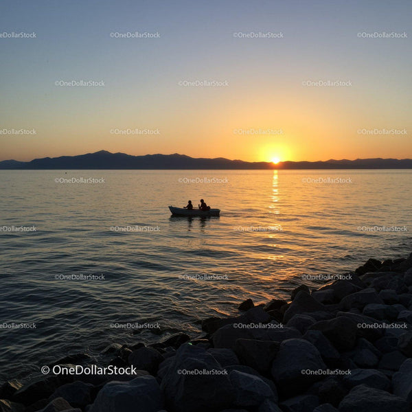 Serene Sunset Over Lake With Small Boat and Mountain Silhouette