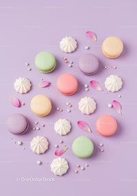 Colorful macarons and meringues with flower petals on purple