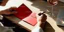 Person writing romantic message in red card with wine glass