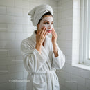 Woman Applying Facial Mask with Towel on Head in Spa Setting