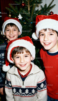 Three boys smiling with Santa hats by Christmas tree