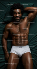 Smiling muscular man relaxing on dark green bed sheets