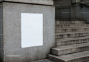 Blank white poster on textured concrete wall near stairs