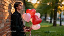 Young man holding heart-shaped balloons and chocolates