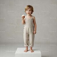 Little child holding cupcake in beige overalls