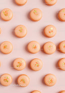Elegant orange macarons with gold flakes on pink background