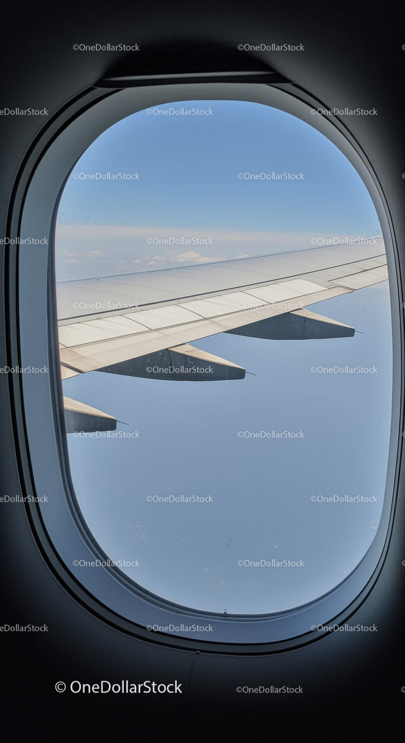 View of an Airplane Wing and Blue Sky Through a Passenger Window