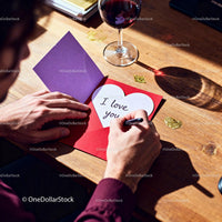 Man Writing Romantic Message in Valentine Card at Table