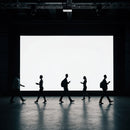 Silhouettes of people walking in front of large screen