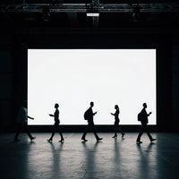 Silhouettes of people walking in front of large screen