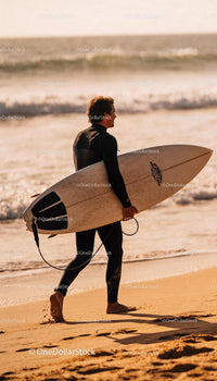 Surfer walking on sandy beach at golden hour