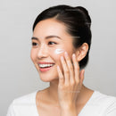Young Woman Applying Moisturizer with a Bright Smile Clear Skin