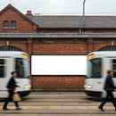 Modern trams passing by blank billboard on brick wall