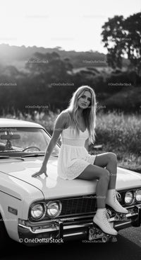 Young woman in white dress sitting on vintage car hood