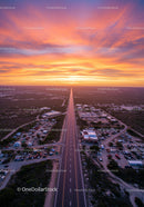 Colorful Sunset Over Long Rural Road with Cars and Buildings