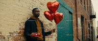 Man holding heart balloons and chocolates outdoors
