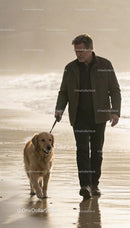 Mature man walking golden retriever on calm beach