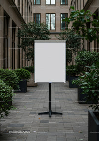 Blank whiteboard in urban courtyard surrounded by greenery