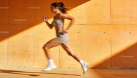 Athletic woman sprinting fast against orange wall