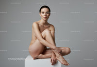 Thoughtful young woman sitting on white block with crossed legs