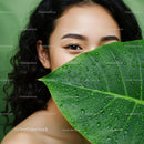 Young Woman with Curly Black Hair and Large Green Leaf with Water Droplets