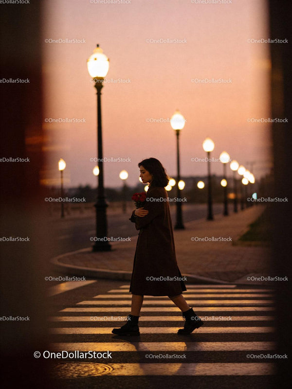 Woman walking alone with roses under streetlights at dusk