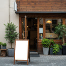 Cozy cafe entrance with blank wooden signboard and plants