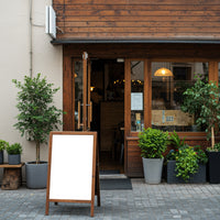 Cozy cafe entrance with blank wooden signboard and plants