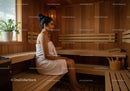 Relaxing Woman Sitting in Wooden Sauna Room with Towel on Her Shoulders
