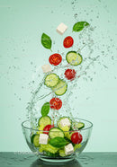 Fresh Greek salad ingredients splashing into glass bowl