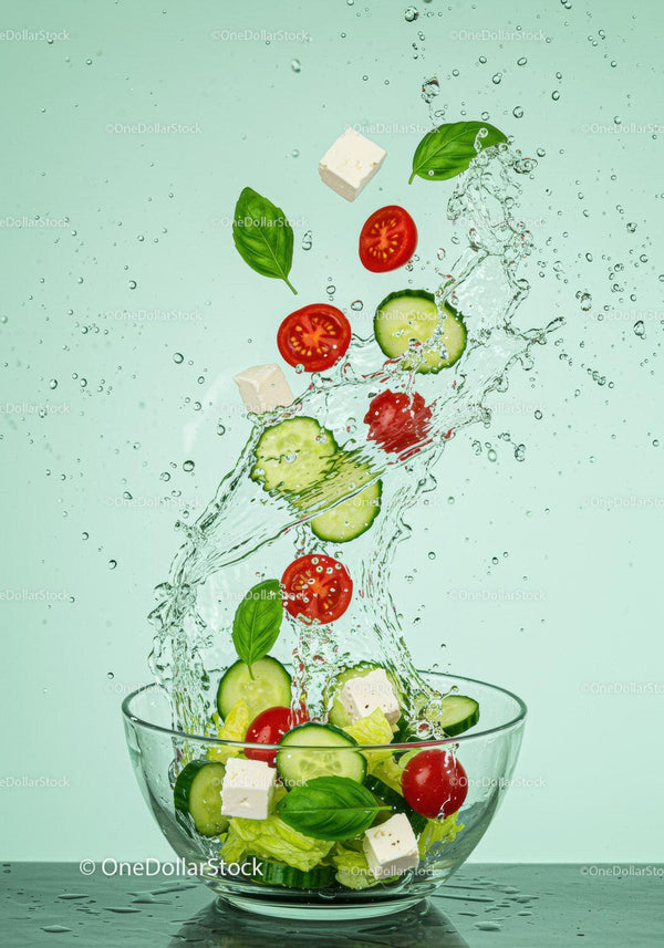 Fresh Greek salad ingredients splashing into glass bowl
