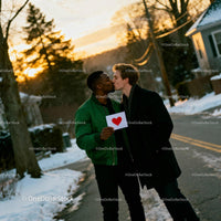 Couple sharing a tender kiss holding heart card outdoors