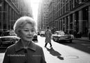 Elderly Woman in Busy City Street Surrounded by Vintage Cars