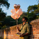 Man holding heart-shaped balloons and chocolates outdoors