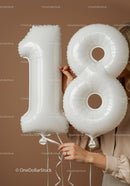 Hands holding white number 18 balloons with beige background