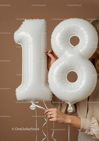 Hands holding white number 18 balloons with beige background