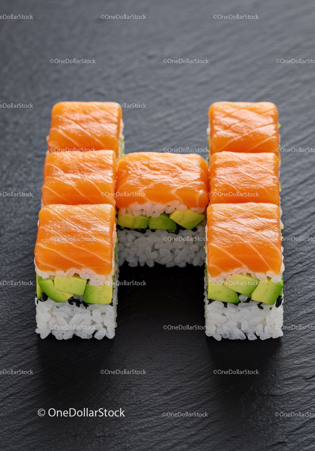 Świeże rolki sushi z łososiem ułożone w literę H na czarnym łupku