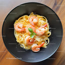 Shrimp Pasta with Basil Garnish on Black Plate in Elegant Dining Setting