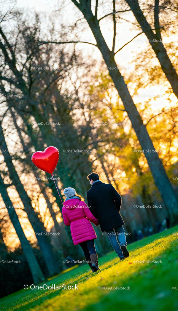 Couple walking in park holding heart shaped balloon