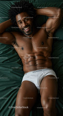 Smiling muscular man relaxing on bed in white underwear