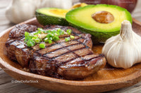 Juicy Grilled Steak with Avocado and Garlic on Wooden Plate