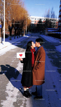 Couple Sharing a Kiss Holding Heart Sign Outdoors
