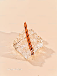Cinnamon Stick Embedded in Clear Ice Cube on Beige Surface