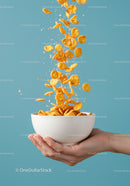 Crispy cornflakes pouring into white bowl held by hand
