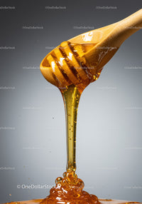 Golden honey slowly dripping from wooden dipper