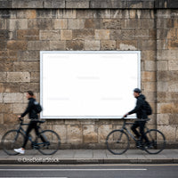 Two cyclists passing blank billboard on stone wall