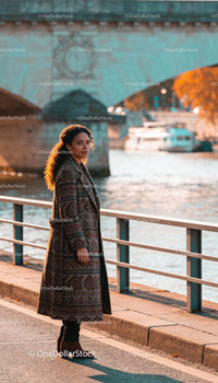 Woman in patterned coat standing by riverside in autumn