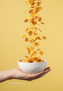 Hand Holding Bowl with Falling Cornflakes on Yellow Background